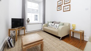 A living room with a sofa, a TV, a wooden coffee table, a lamp, and framed pictures on the wall. - JOIVY The Old Town Sugar House - Amazing Location (Edinburgh)