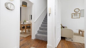 A hallway with a wooden floor, a staircase, a dining area with a table and chairs, and a living area with a sofa and a small table. - JOIVY The Old Town Sugar House - Amazing Location (Edinburgh)