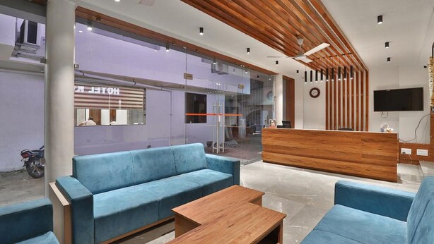 A modern hotel lobby with blue sofas, a wooden reception desk, and a large TV screen. - Hotel Kuber by Sky Stays (Dwarka)