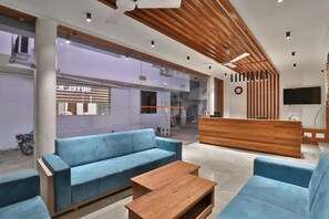 Een moderne hotellobby met blauwe banken, een houten receptiebalie en een groot televisiescherm.