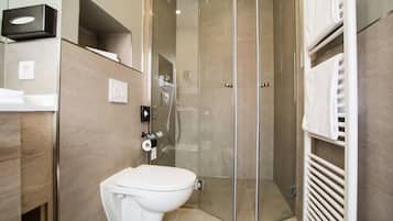 Uma casa de banho moderna com sanita, cabine de duche com paredes de vidro e um porta-toalhas.