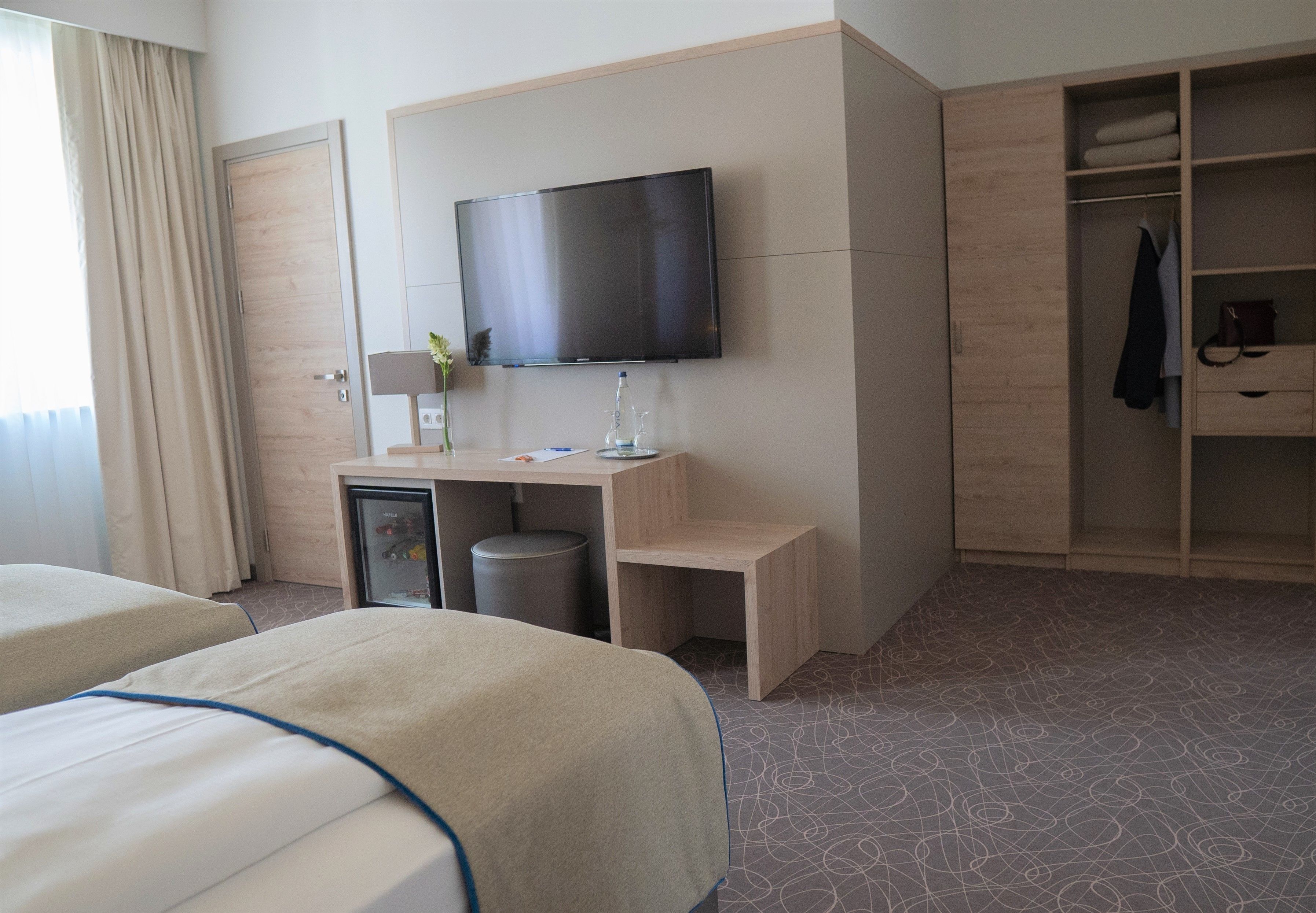 Una habitación de hotel con dos camas, un escritorio con televisor, un armario y un cesto de basura.