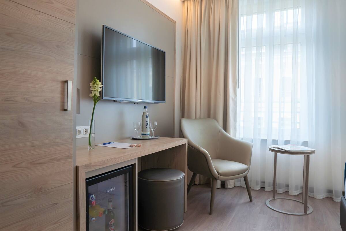 Une chambre d’hôtel moderne équipée d’un téléviseur à écran plat fixé au mur, d’un bureau en bois agrémenté d’un vase de fleurs, d’une chaise, d’une petite table et d’une poubelle.