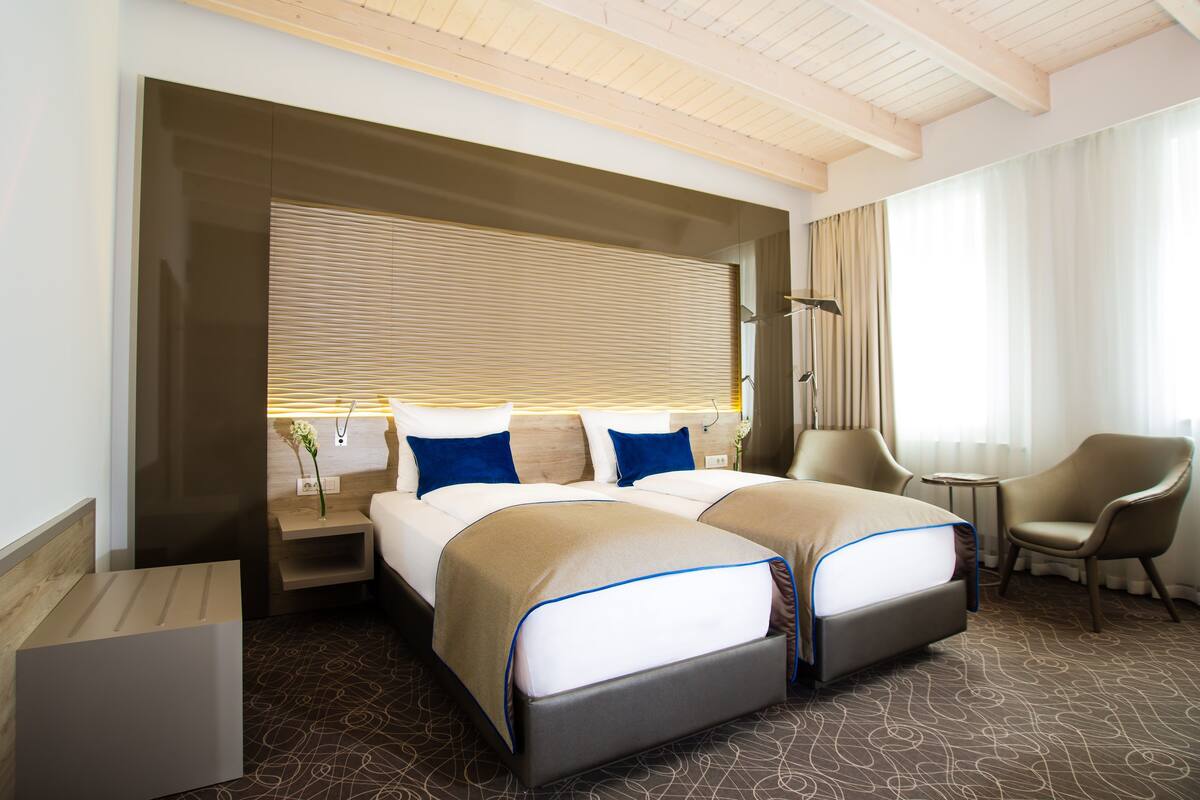 Une chambre d’hôtel avec deux lits, un coin salon et une grande fenêtre avec des rideaux.