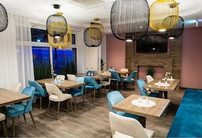 Een restaurant met meerdere tafels en stoelen, een open haard en hangende吊り下げ型 ランプ.
