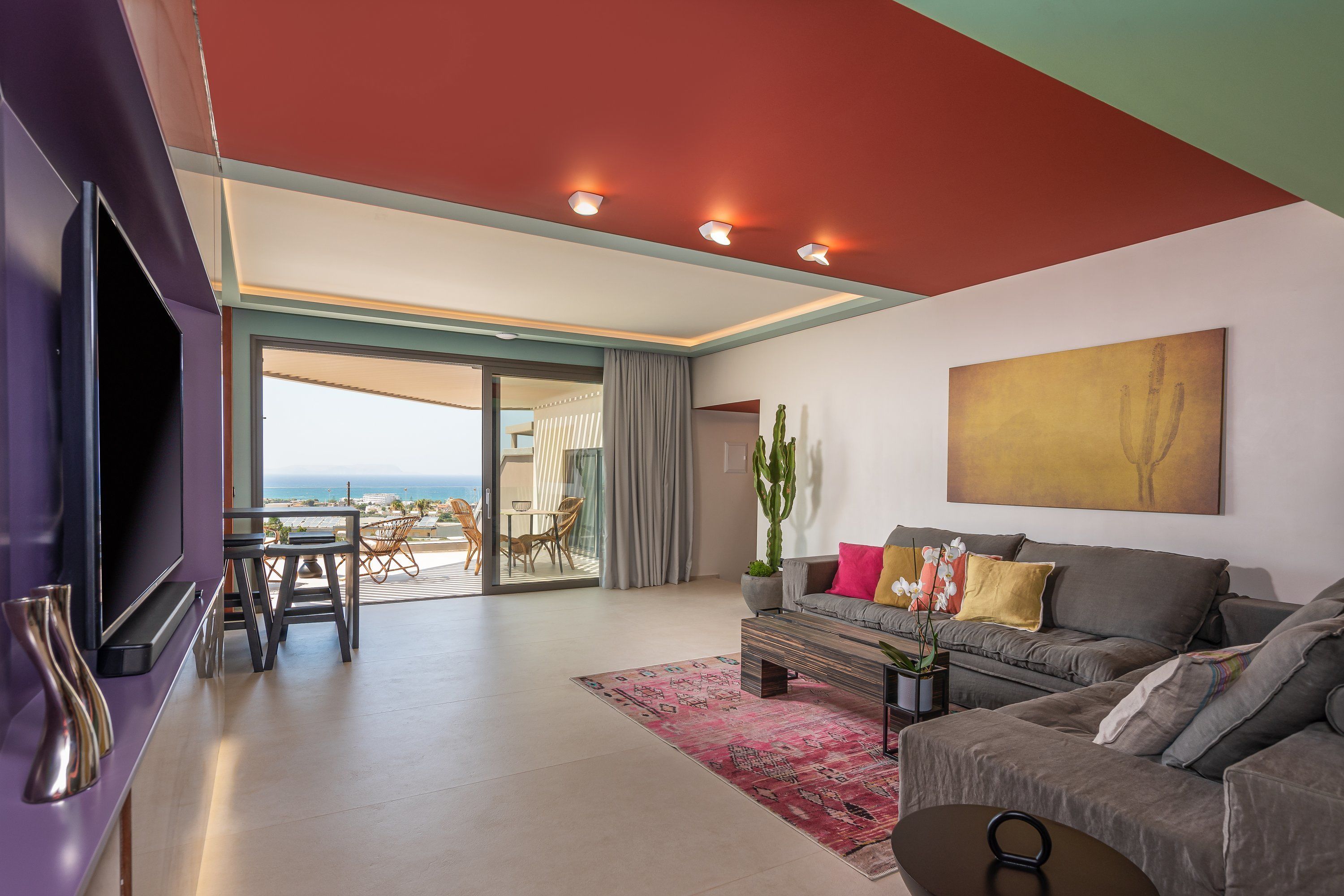 A modern living room with a large flat-screen TV, a grey sofa, a coffee table, and a red ceiling.
