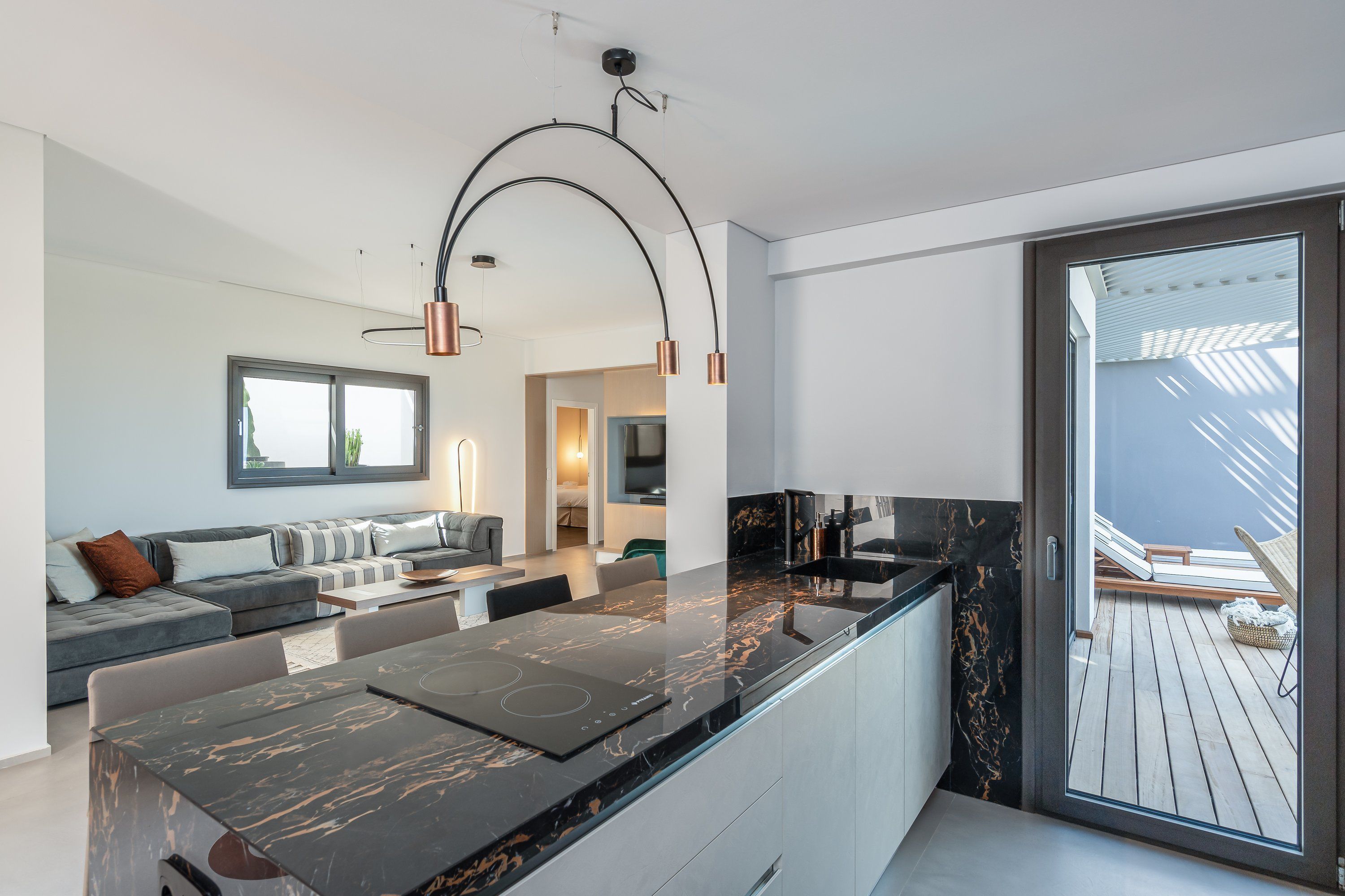 A modern kitchen with a black marble countertop, a built-in oven, and a large window overlooking a wooden deck.