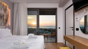 A modern hotel room with a large bed, a balcony with a city view, a wooden bench, and a round mirror. - Onira Suite Dreams (Hersonissos)