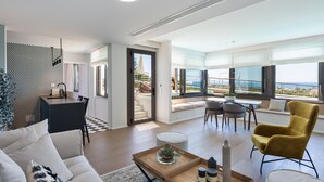 A spacious living area with a sofa, a yellow armchair, a dining table, and a kitchen area with a view of the sea. - Onira Suite Dreams (Hersonissos)