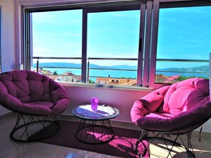 Una habitación con dos sillones rosa, una pequeña mesa redonda y vistas a un cuerpo de agua y montañas a través de amplios ventanales.