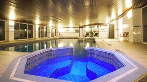 Una piscina interior con borde de azulejos, techo de madera y una zona de estar con sillas.