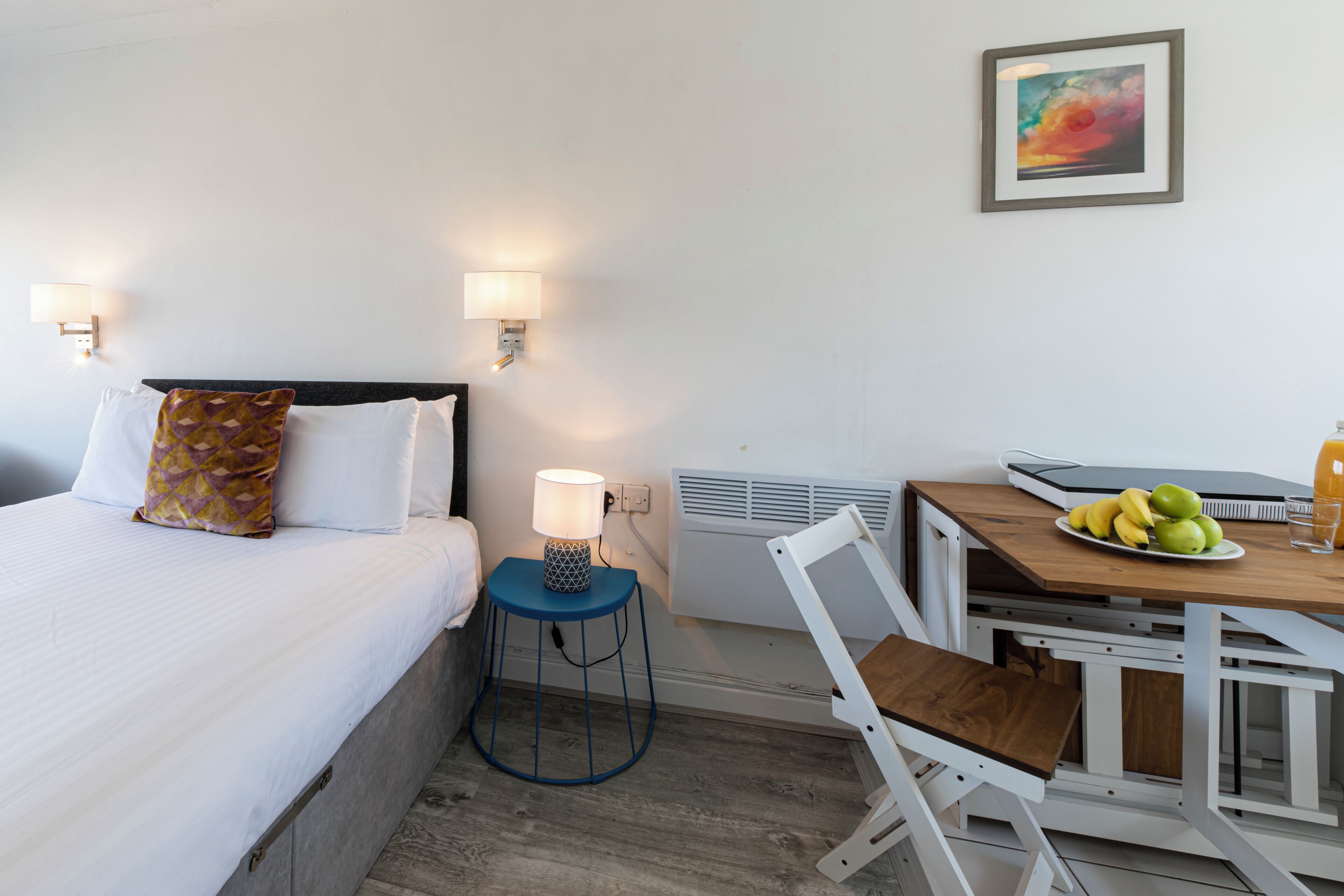 Ein Hotelzimmer mit Bett, Nachttischlampe, Tisch mit Früchten und einem Sessel.