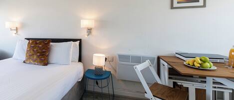 Ein Hotelzimmer mit Bett, Nachttischlampe, Tisch mit Früchten und einem Sessel.
