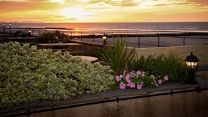 Vista del atardecer desde un balcón con barandilla, que da a una playa y al océano.