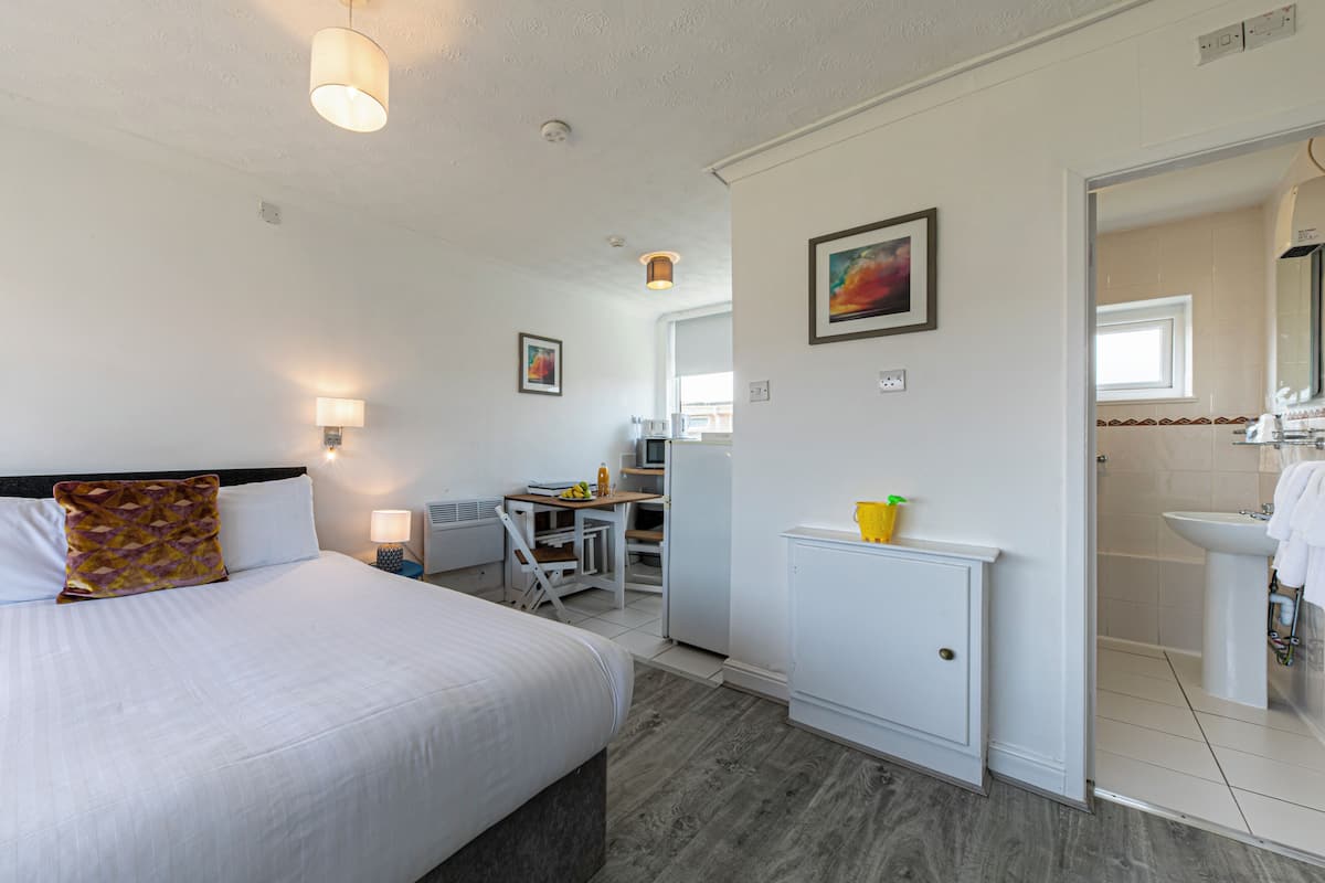 A hotel room with a bed, desk, and kitchenette.