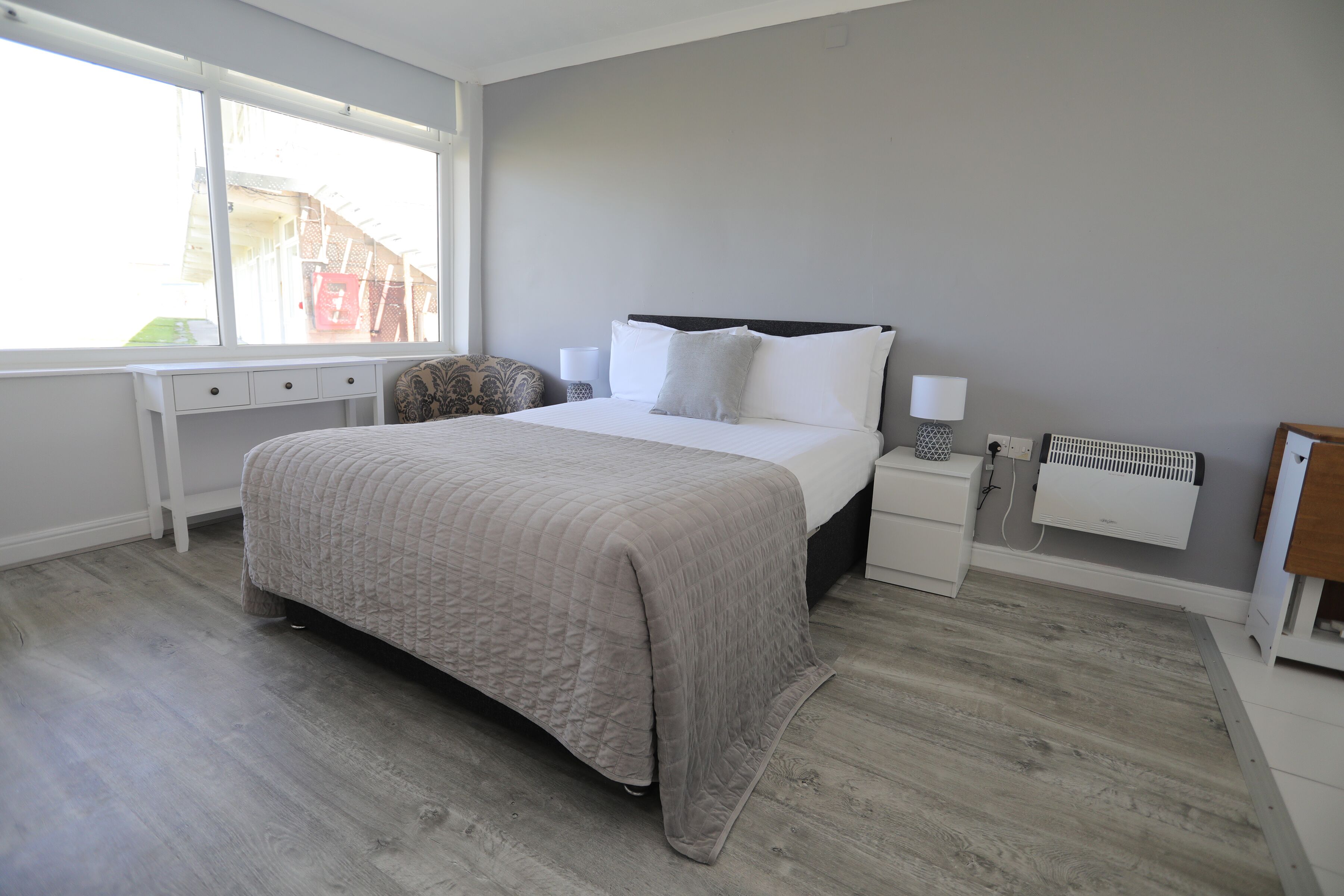 Een slaapkamer met een bed, nachtkastjes, een bureau en een radiator.