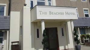 Un hotel llamado "The Beaches Hotel" con una entrada destacada, amplias ventanas y plantas en macetas.