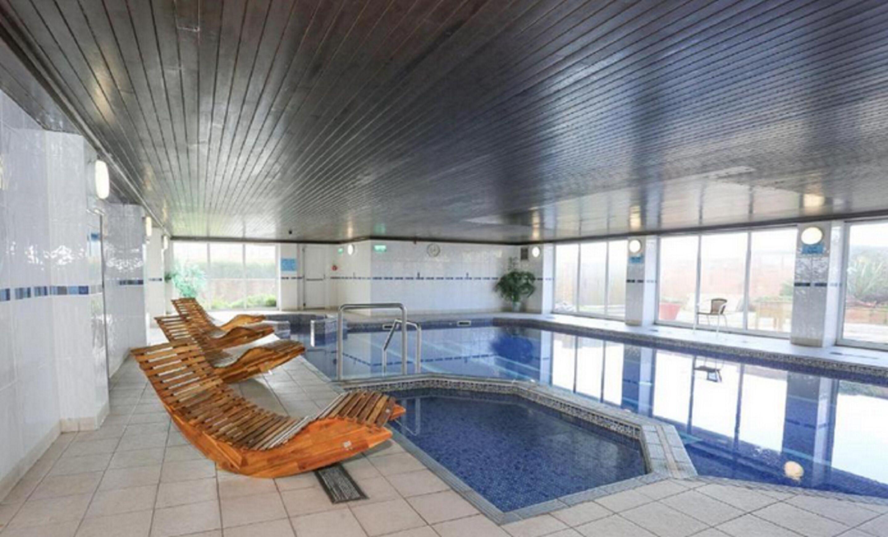 Una piscina interior con tumbonas de madera y suelo de baldosas.