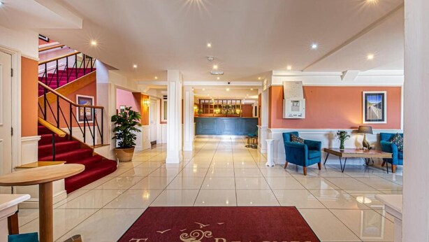 Un vestíbulo de hotel con alfombra roja, una escalera, un mostrador de recepción y una zona de bar.