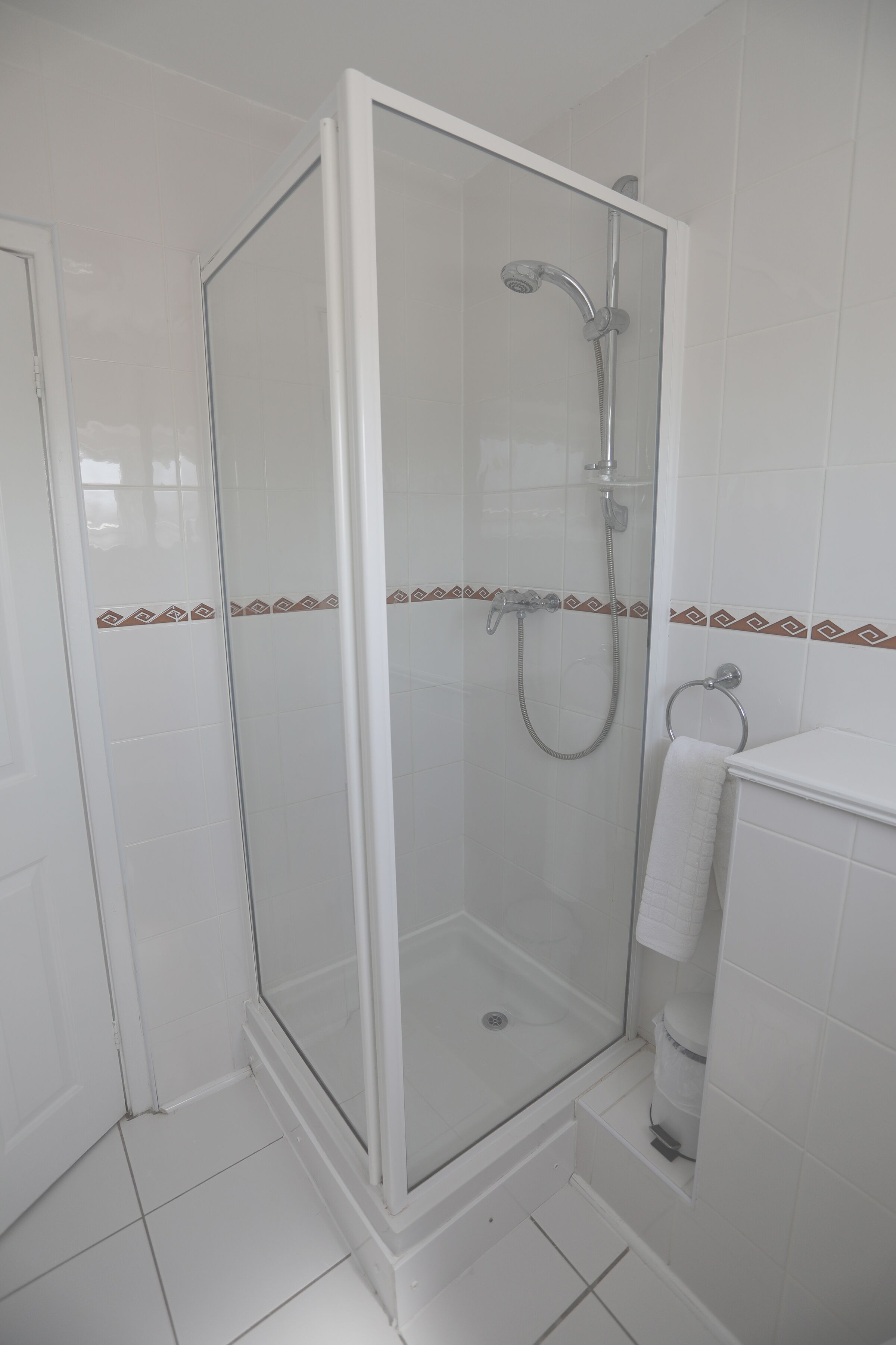 Un espacio de ducha con puerta de vidrio, cabezal de ducha de mano y barra para toallas.
