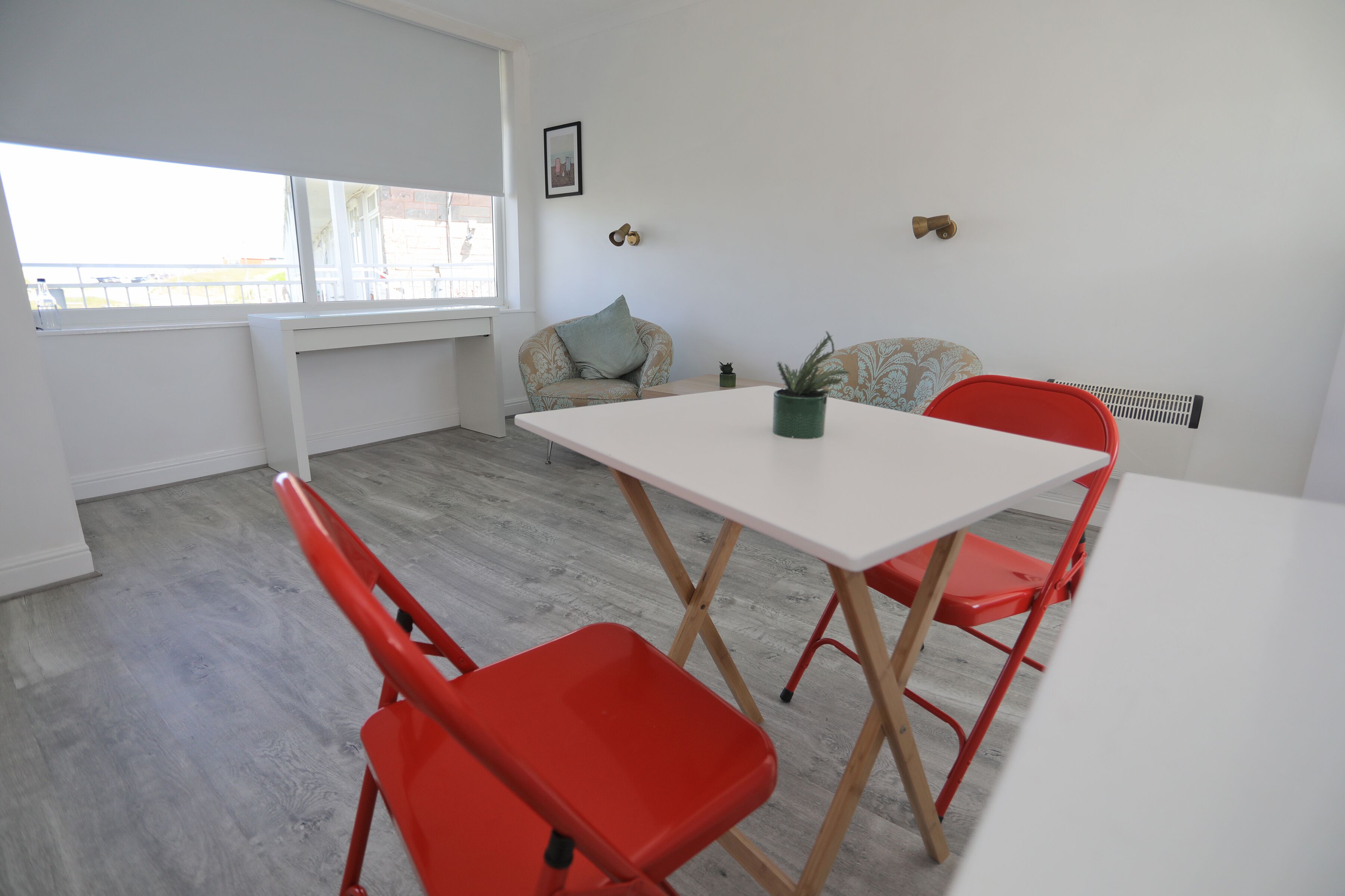 Une pièce avec une table blanche et des chaises rouges, une fenêtre donnant sur un paysage agréable et un radiateur fixé au mur.