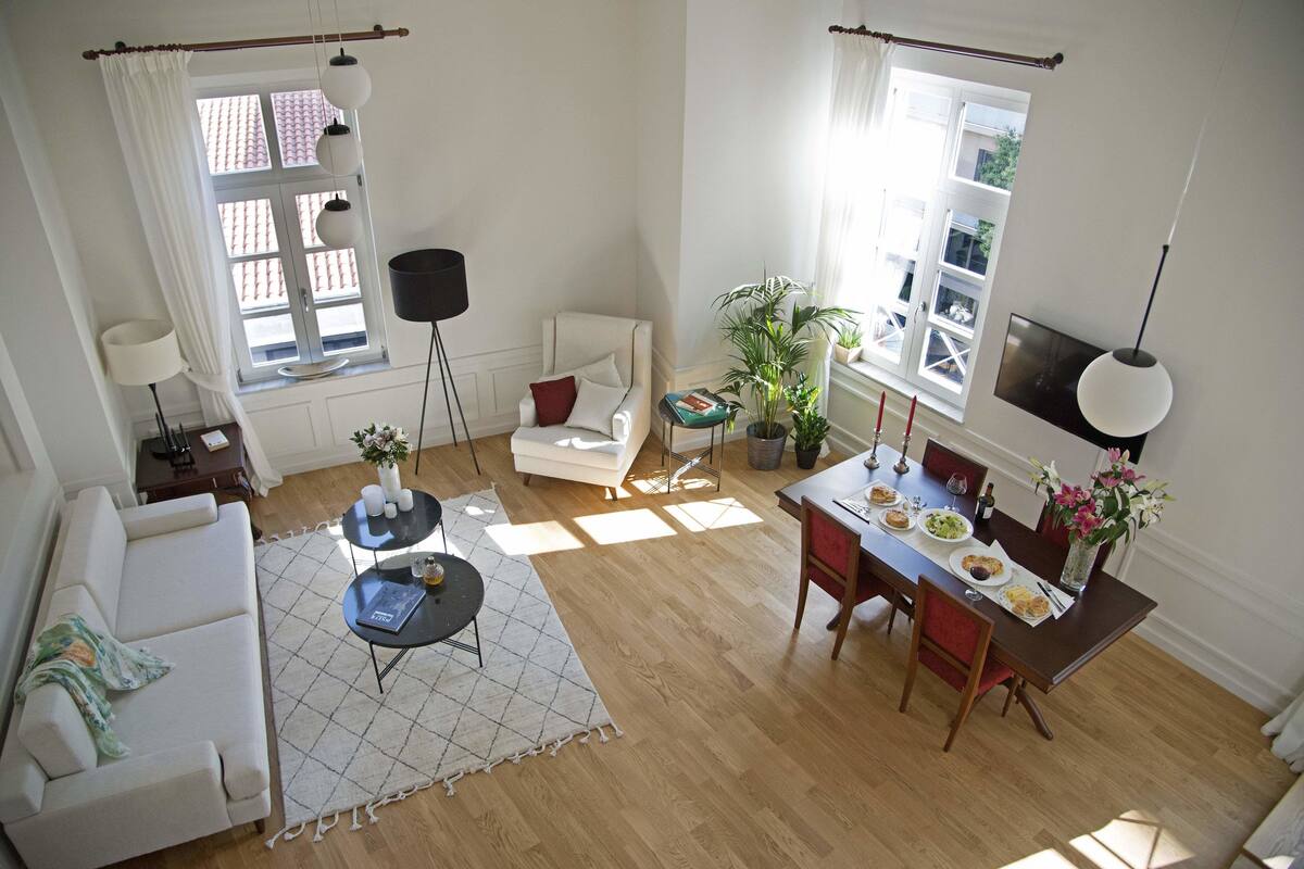 A spacious living room with a sofa, a dining table set with plates, and a TV mounted on the wall.