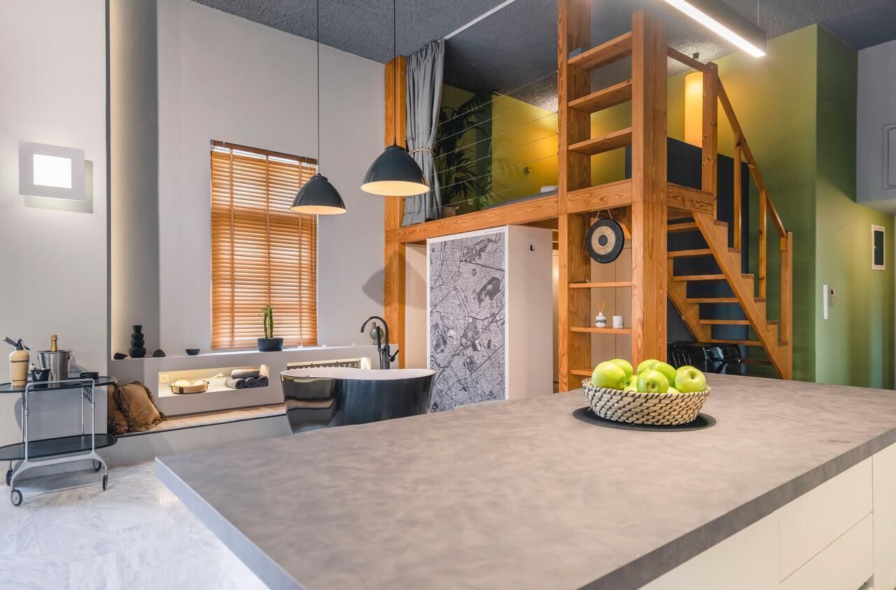A modern kitchen with a central island, wooden staircase, and pendant lighting.