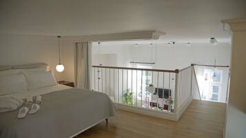 A bedroom with a large bed, a balcony with a railing, and a view of the outside.