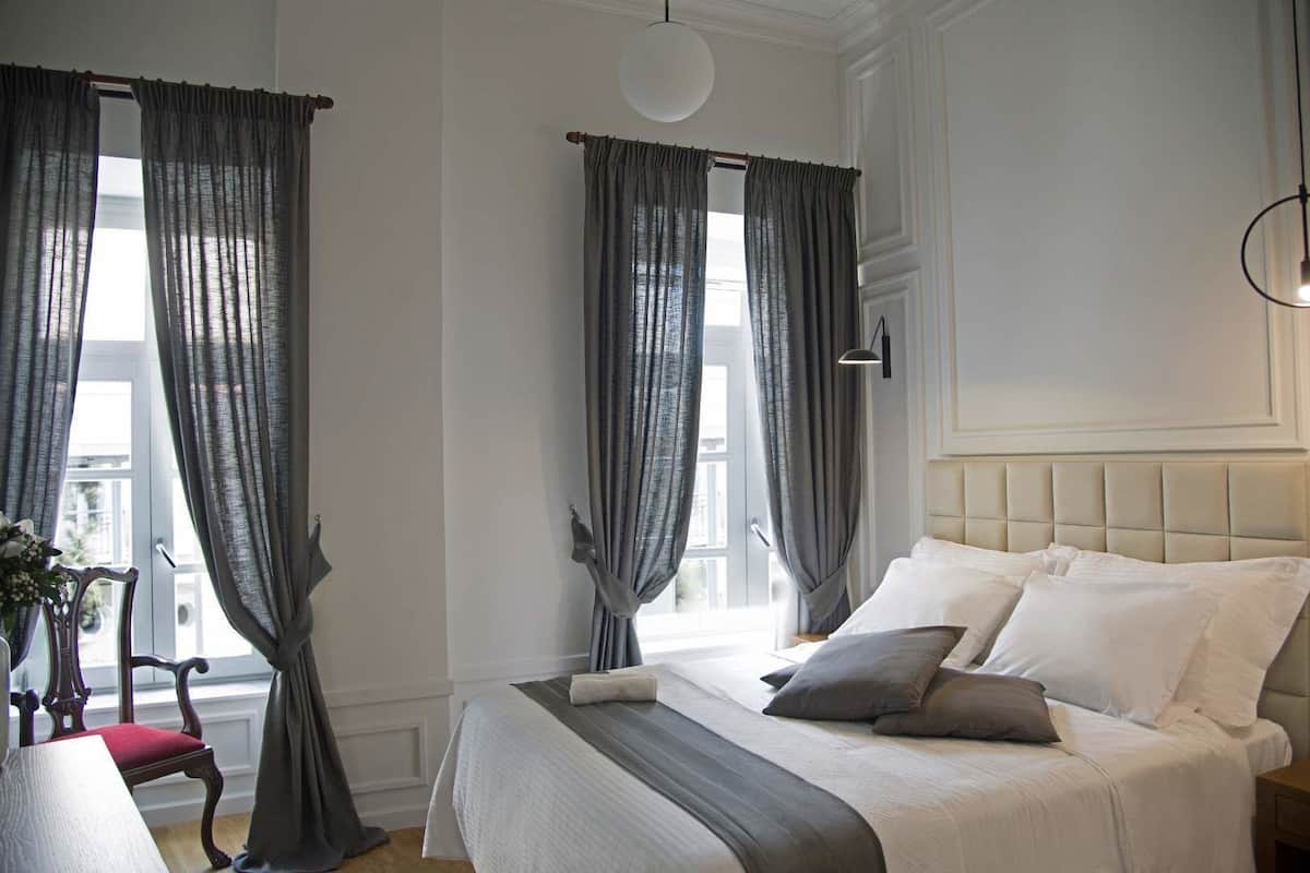 A bedroom with a bed, curtains, a bedside table, and a chair.