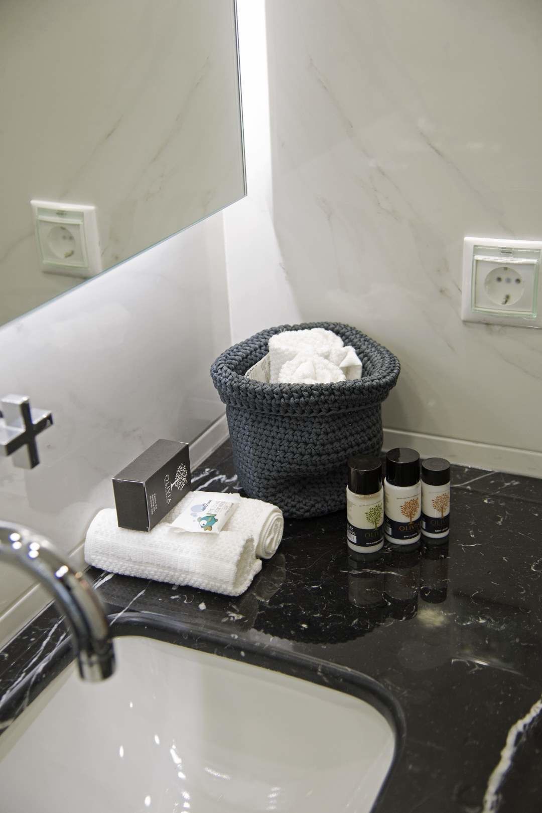A bathroom with a marble sink, a towel, a basket, and two bottles of olive oil.