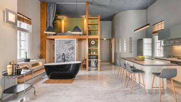 A modern kitchen with a large island, a black bathtub, and a loft area with a wooden ladder.