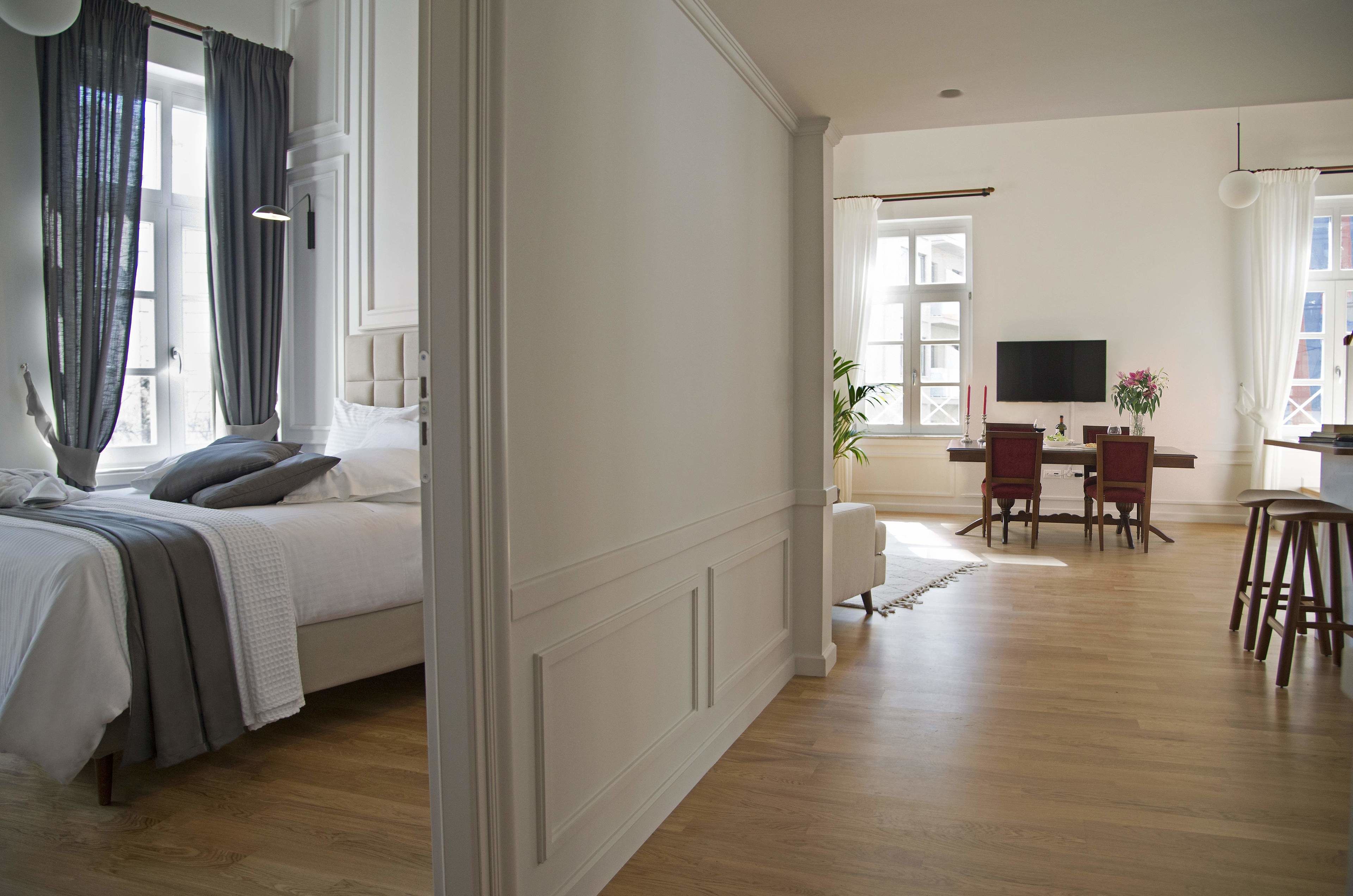 A spacious room with a bed, a dining area with chairs and a table, and a television on the wall.