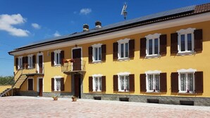 A yellow building with multiple windows, a balcony, and a paved courtyard. - Agriturismo Cà del Nono (Moasca)