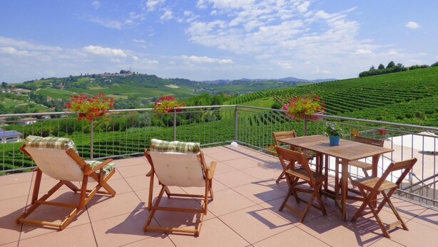 A terrace with a table and chairs, overlooking a vineyard and a distant hill. - Agriturismo Cà del Nono (Moasca)