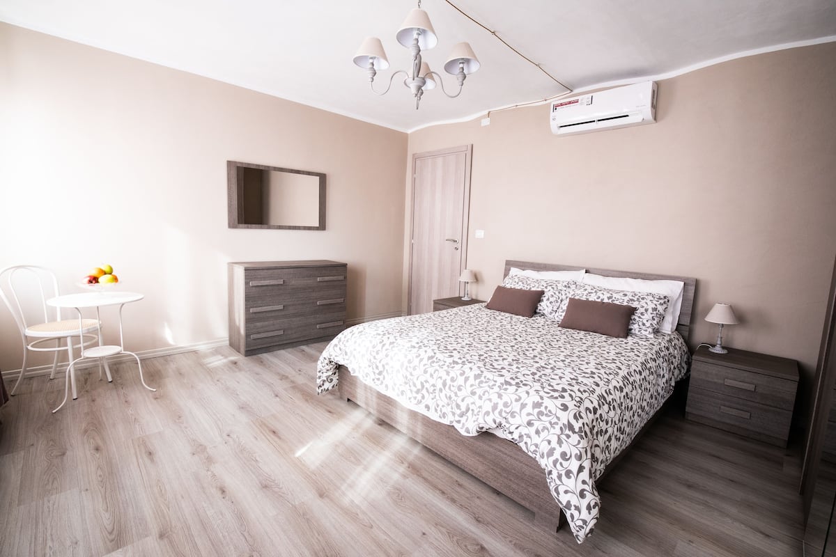A bedroom with a bed, bedside table, chair, dresser, and a small table with fruit.