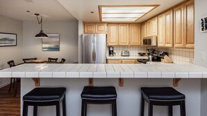 Une cuisine moderne avec des meubles en bois, un réfrigérateur en acier inoxydable, un four à micro-ondes et un grand îlot central doté de tabourets de bar.