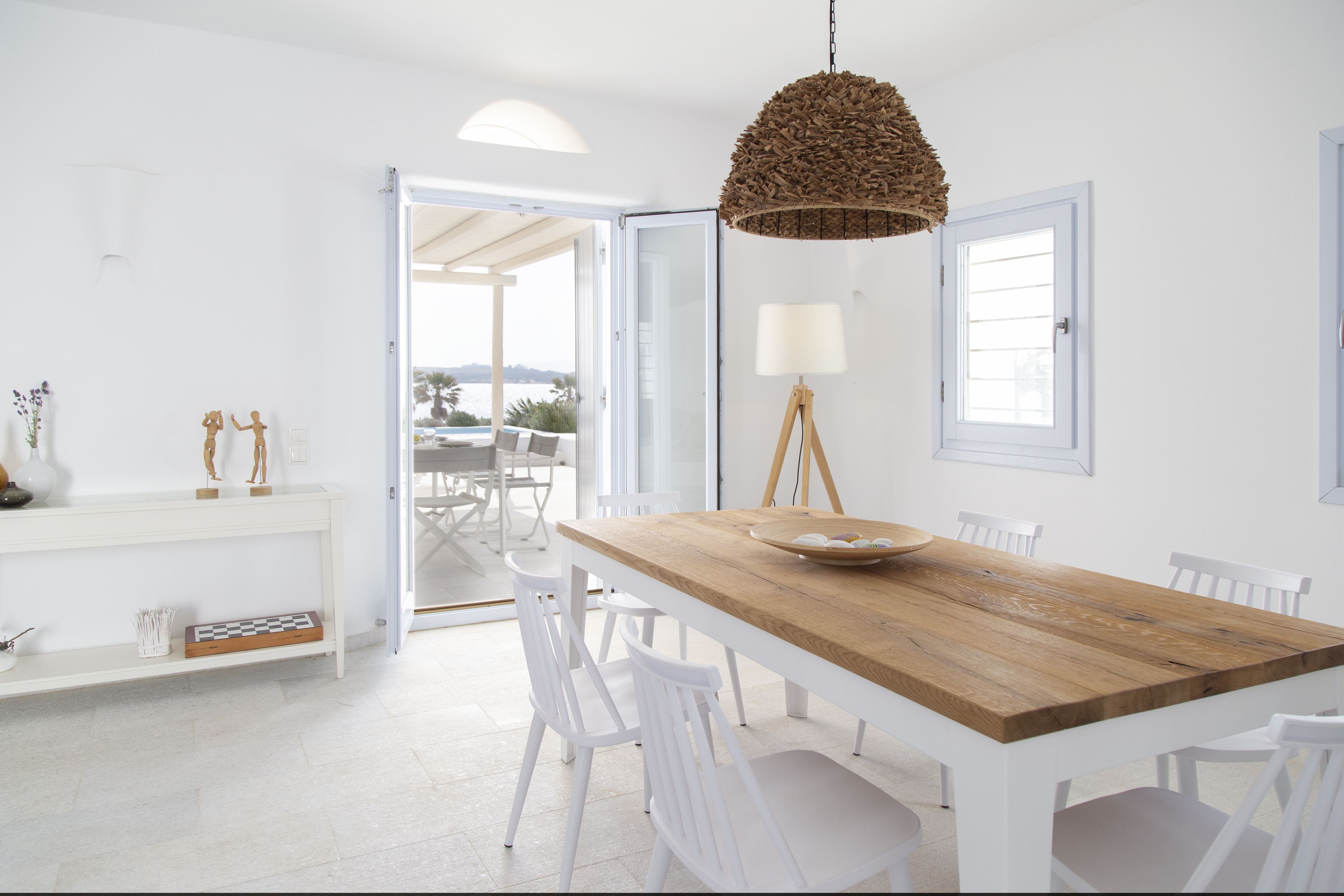 Un comedor amplio y luminoso con una mesa de madera, sillas blancas y una lámpara colgante de mimbre.