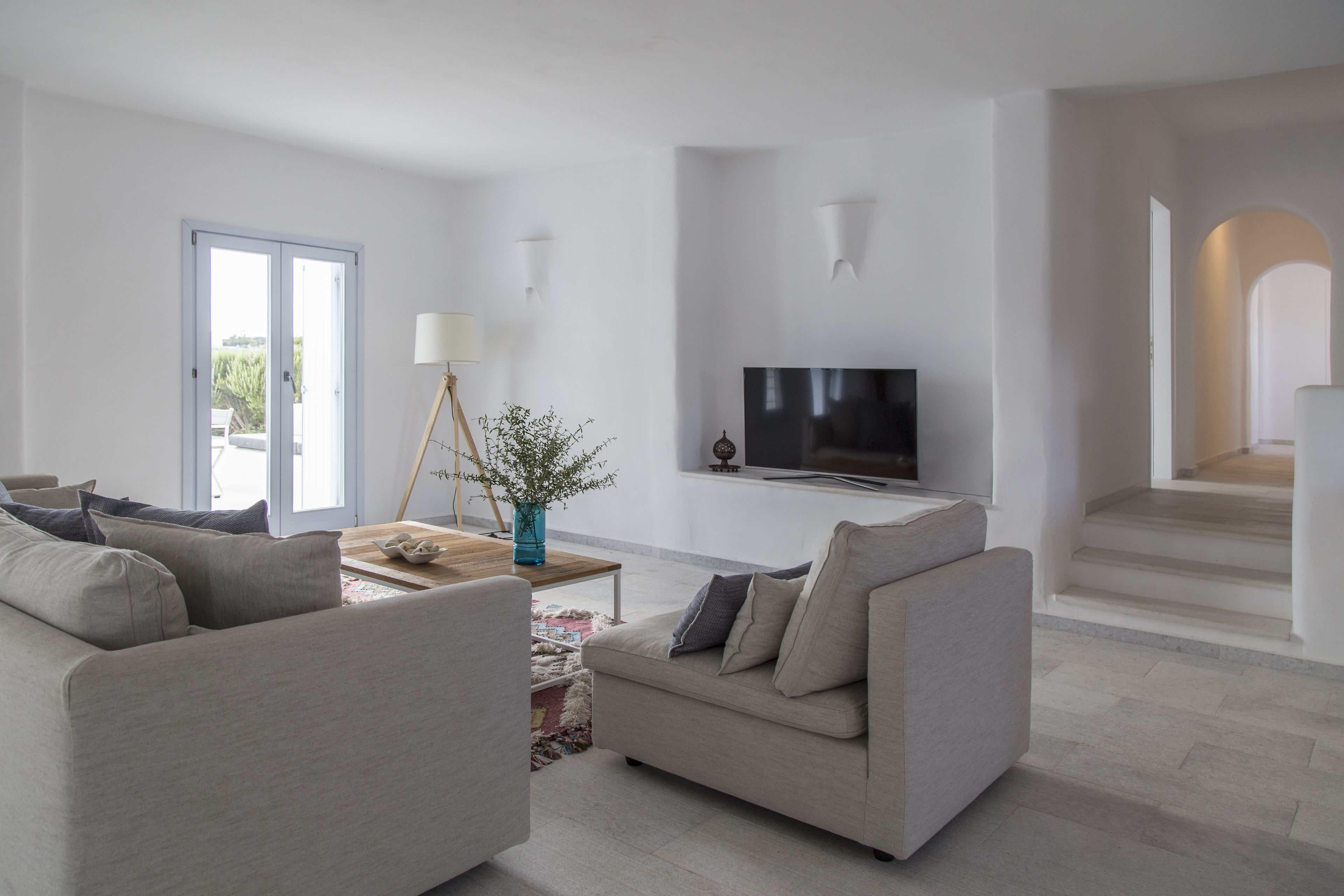 Een moderne woonkamer met een bank, een salontafel en een televisie. Een deur leidt naar een balkon en er is een trap op de achtergrond.