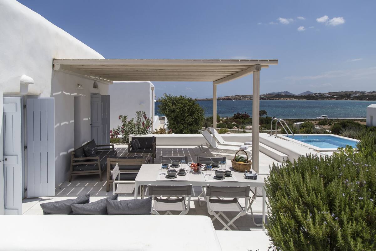 A terrace with a table set for dining, a pool, and a view of the sea.