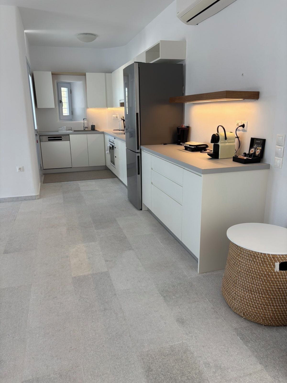 A modern kitchen with white cabinetry, a stainless steel refrigerator, a built-in oven, and a small island with a coffee machine.