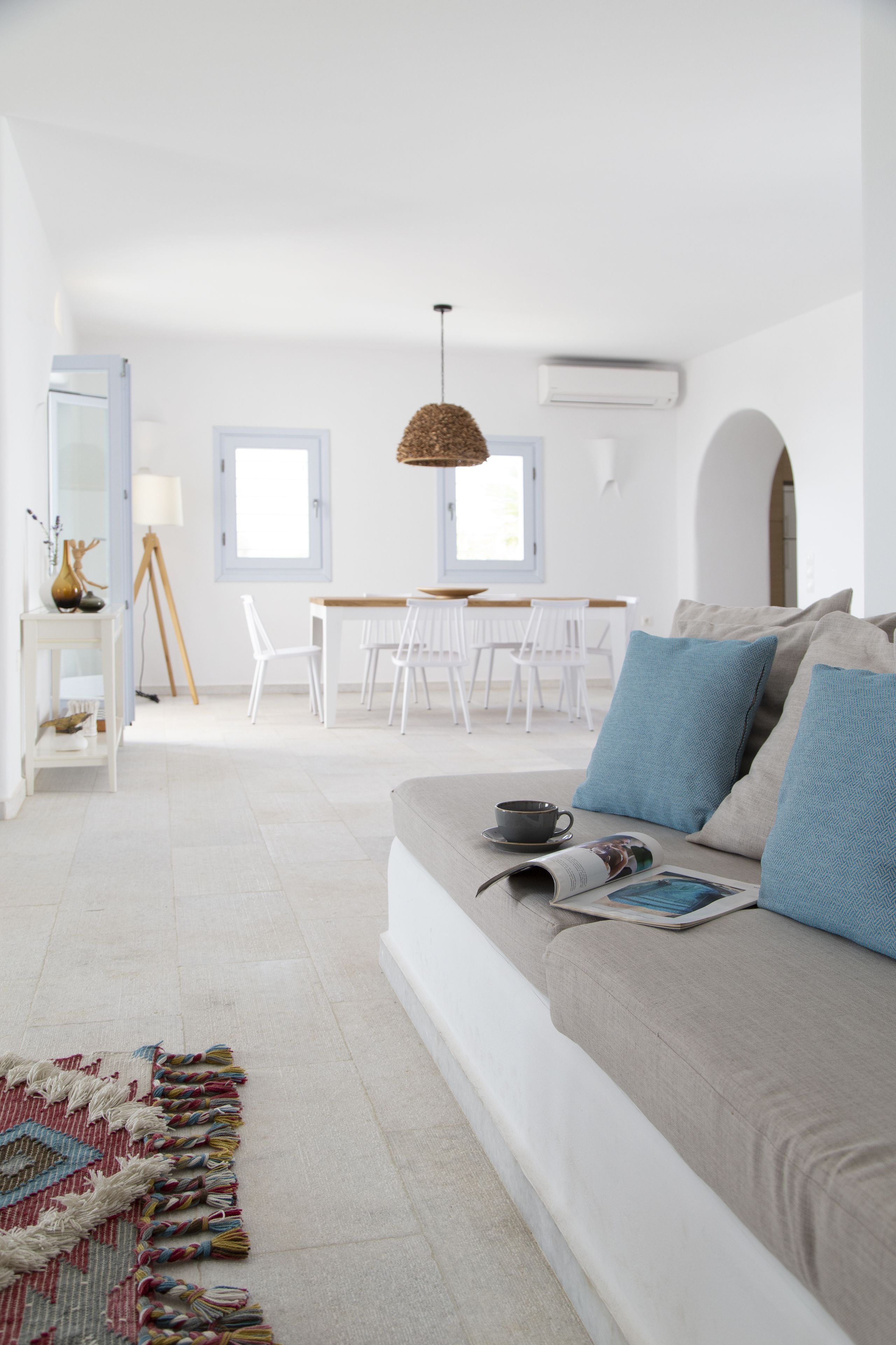 En moderne stue med sofa, spiseområde med stole, lampe og hængende lysarmatur.
