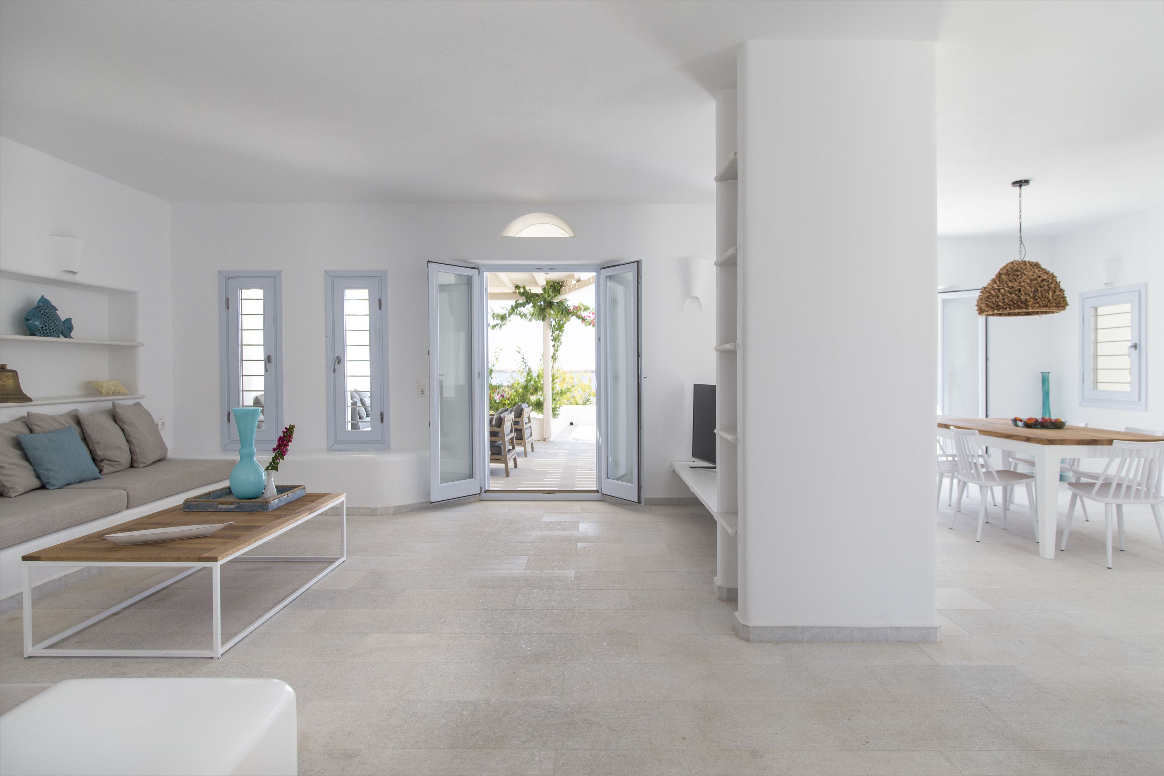 A modern living room with a sofa, coffee table, and open doors leading to a dining area with a table and chairs.
