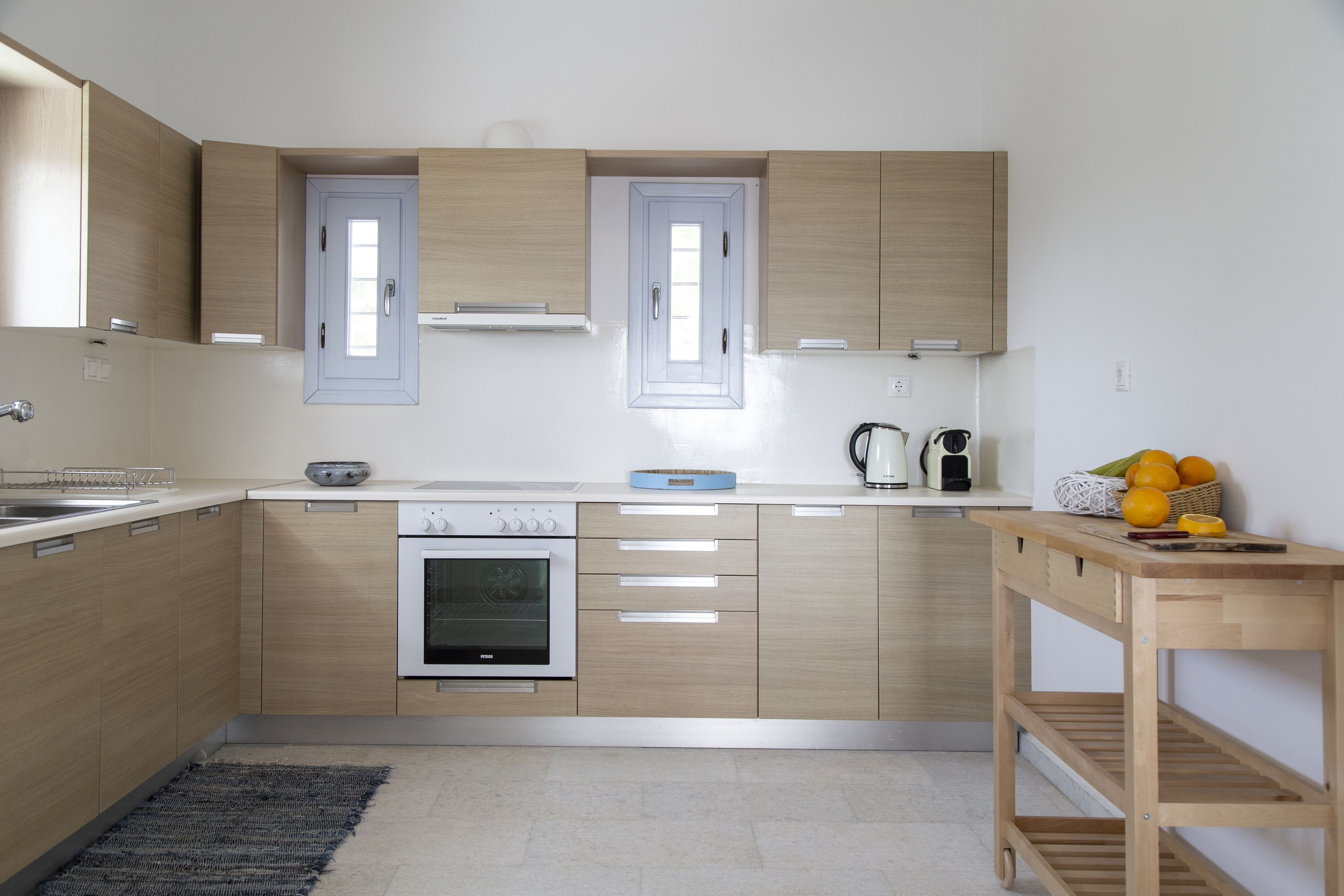 A modern kitchen with wooden cabinets, a built-in oven, and a small table with fruits.