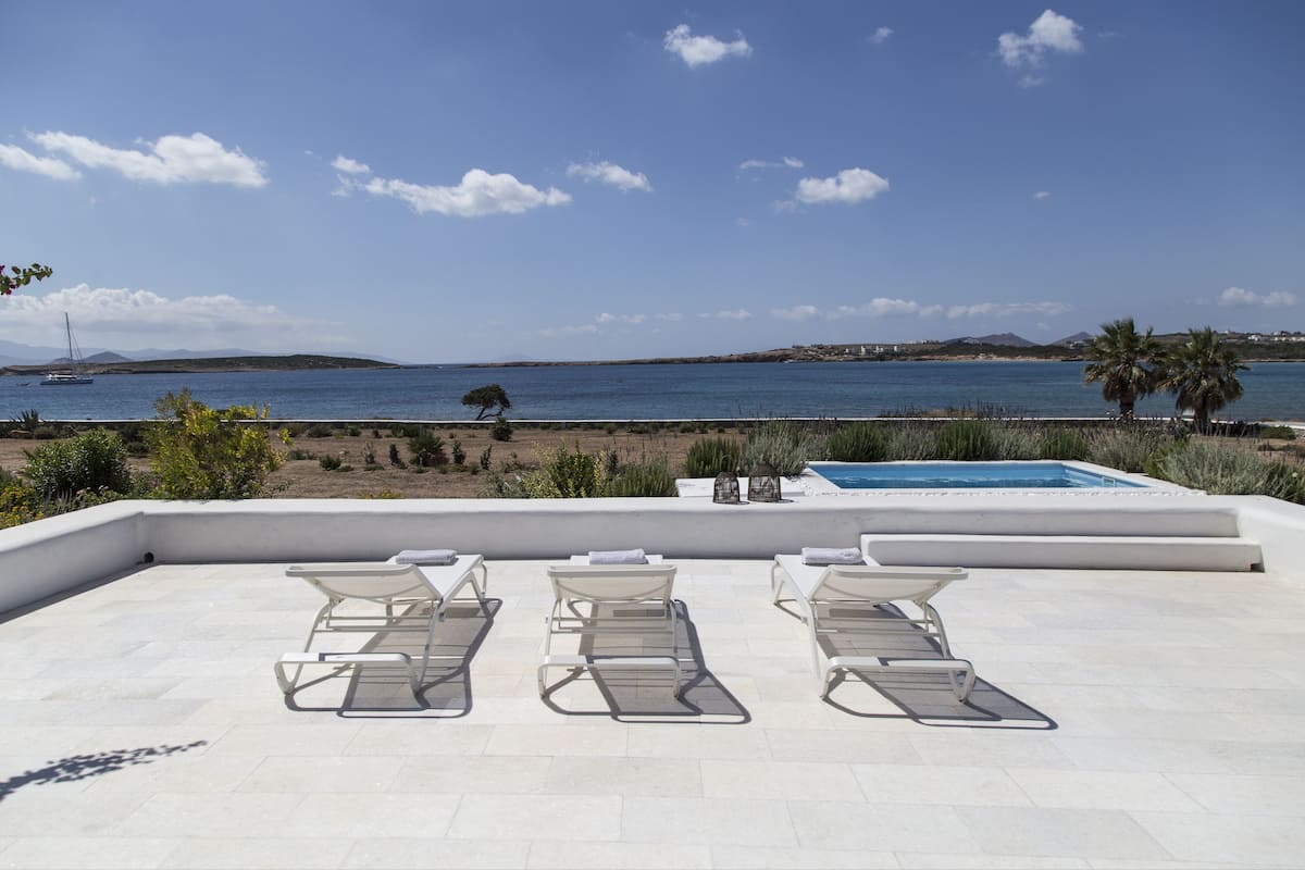 A rooftop pool area with three sun loungers, a small pool, and a view of the sea and distant hills.