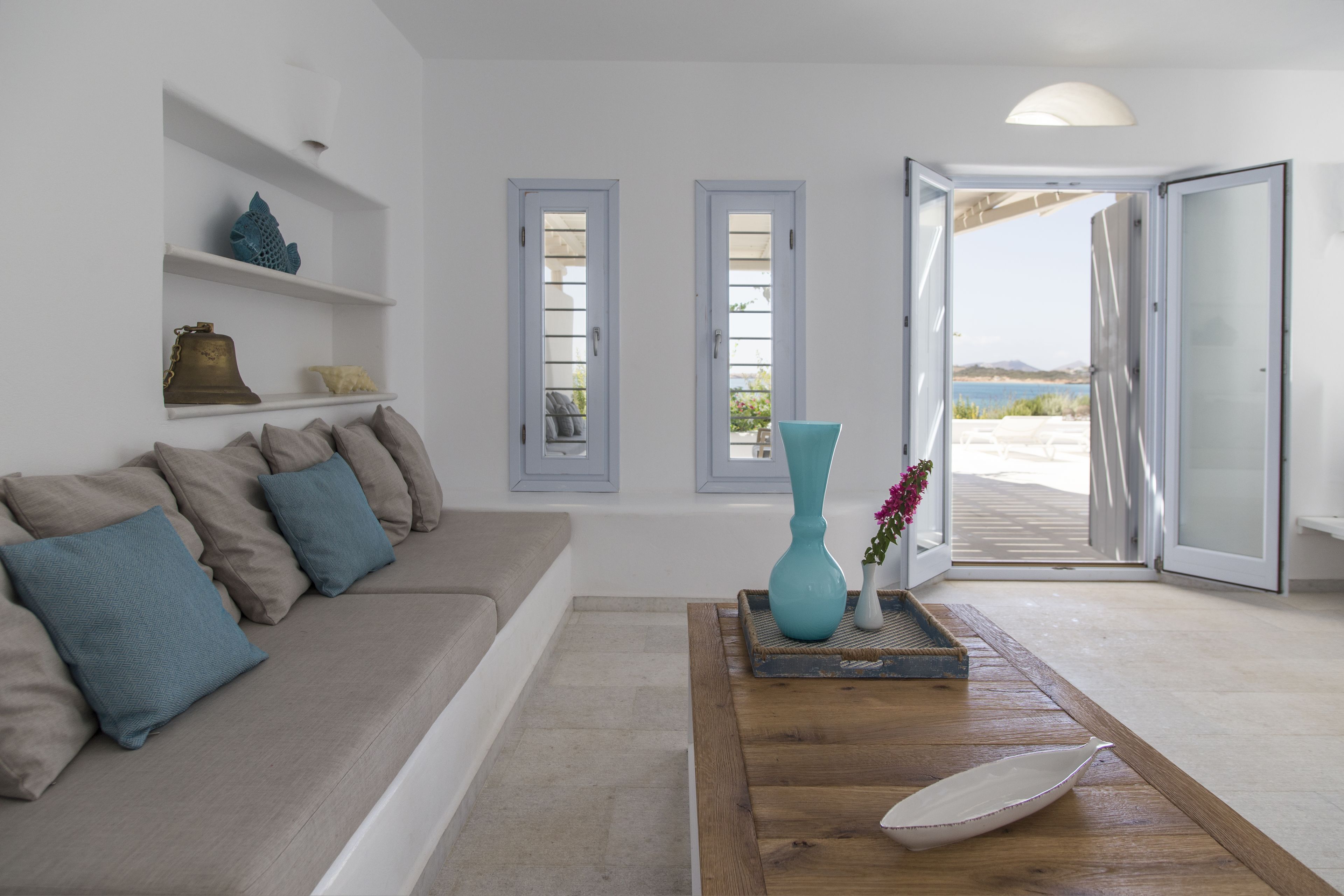 A modern living room with a beige sofa, a wooden coffee table, and a view through an open door to an outdoor area.