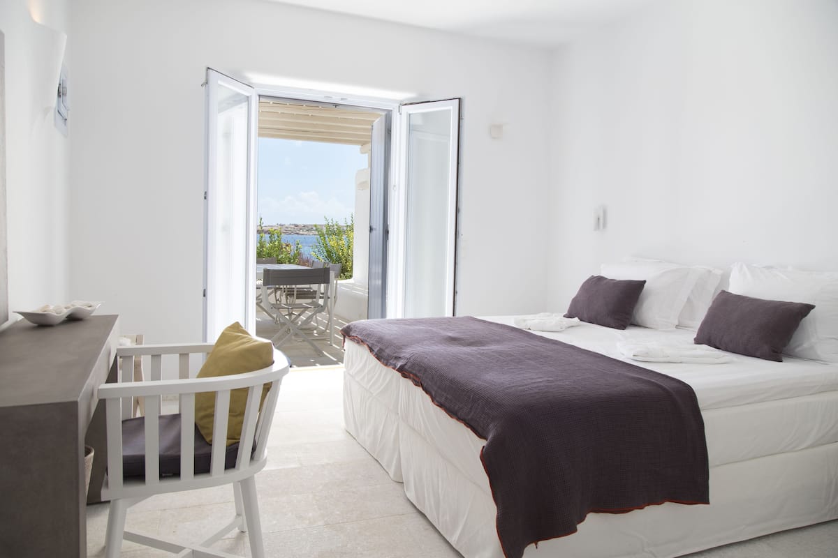 A bedroom with a bed, a desk, and a chair. There is a window with a view of the outdoors.