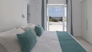 A bedroom with a bed, pillows, and a view of the outdoors through an open door. - The Sand Collection (Paros)