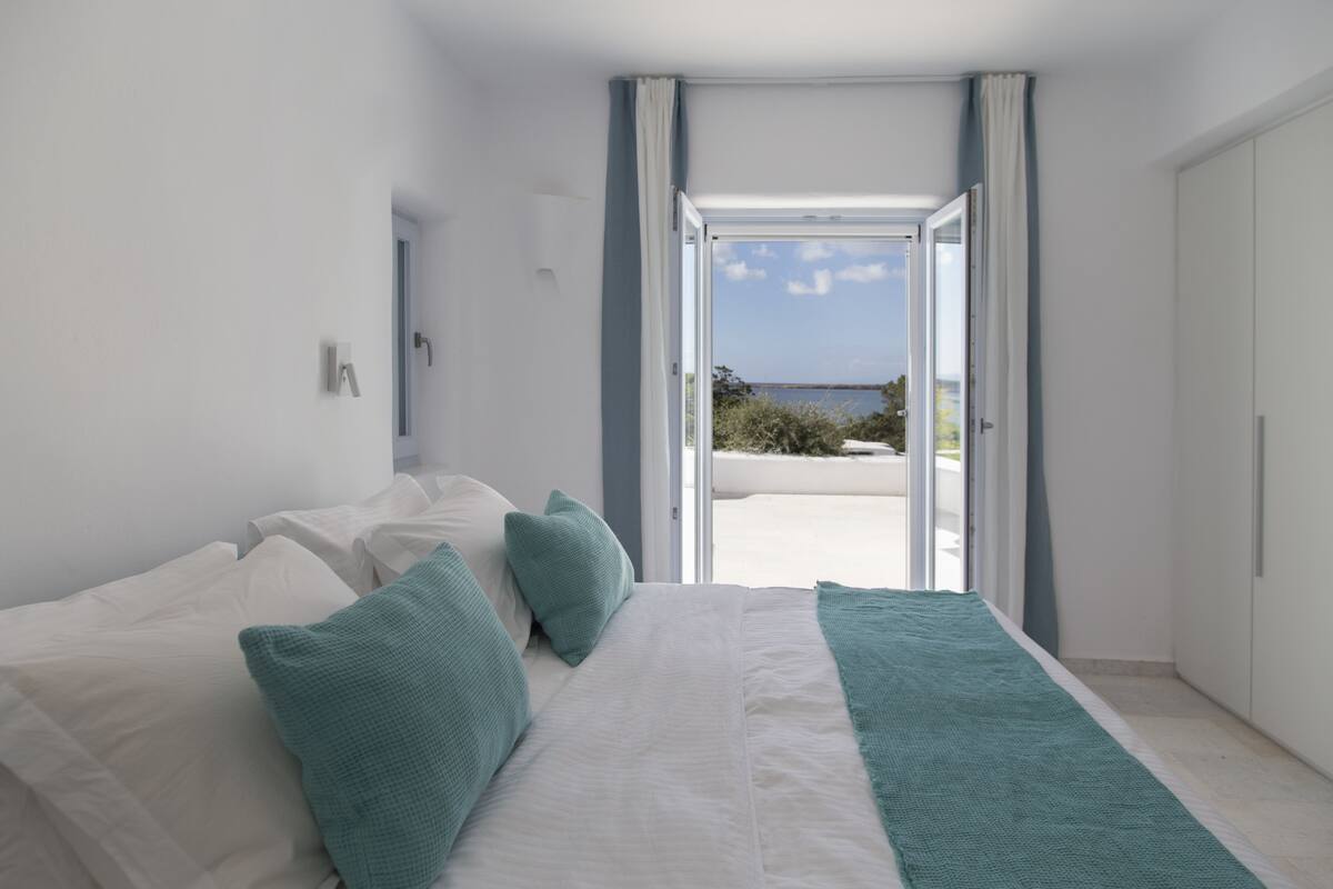 A bedroom with a bed, pillows, and a view of the outdoors through an open door.