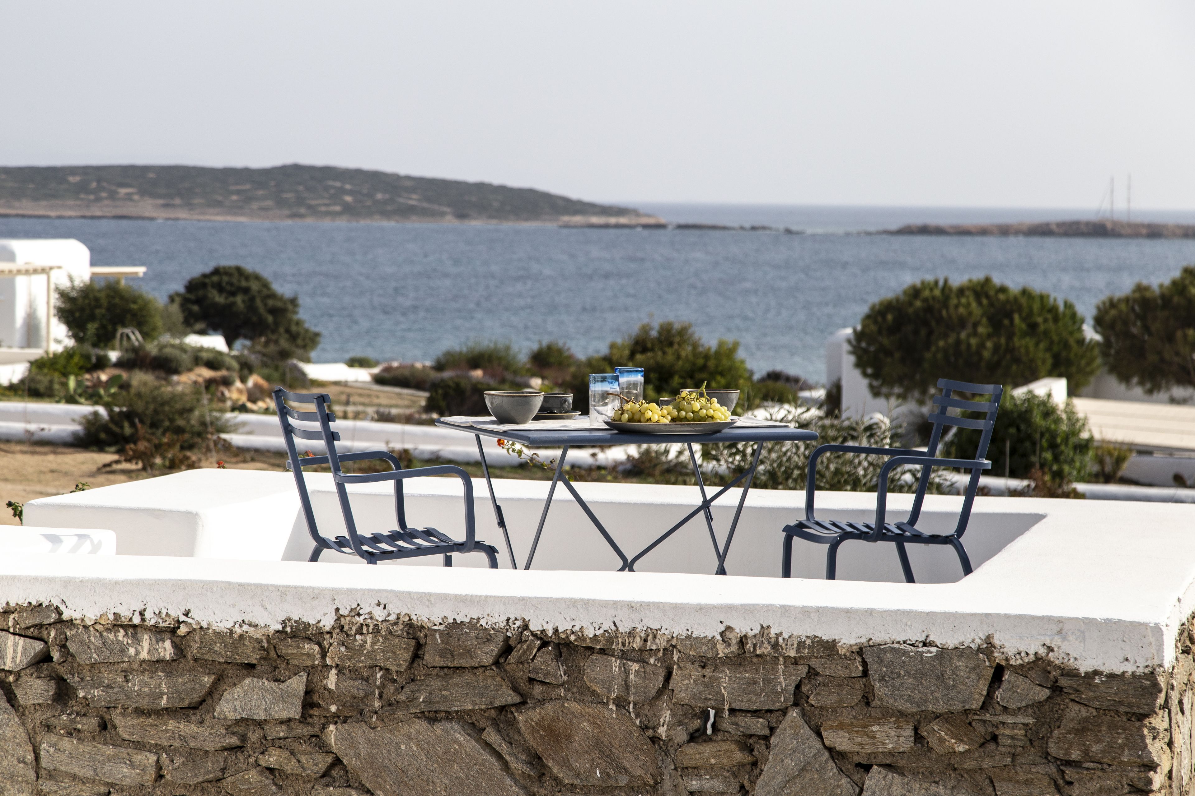 An outdoor dining area with a table and chairs, overlooking a body of water and a distant view of a bridge.