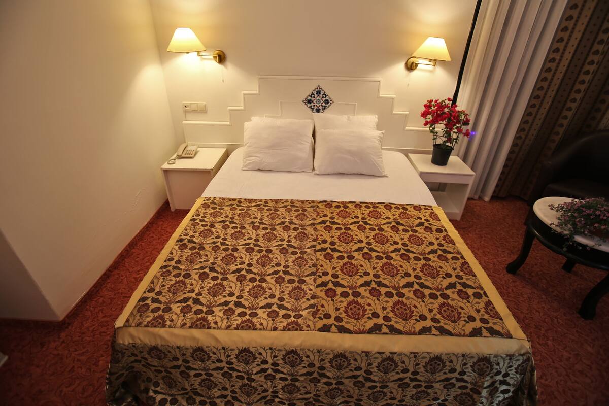 Une chambre d’hôtel avec un grand lit, deux lampes de chevet, une table de chevet, une chaise et une plante en pot.